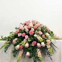 A pink and white casket cover designed with lush, fresh flowers.